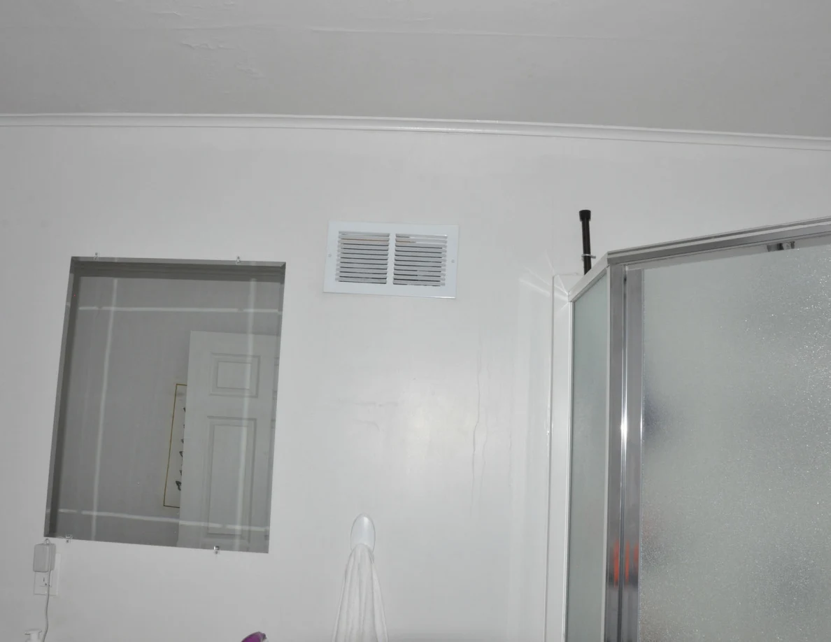 Bathroom wall with mirror, vent and the edge of a frosted-glass shower enclosure.