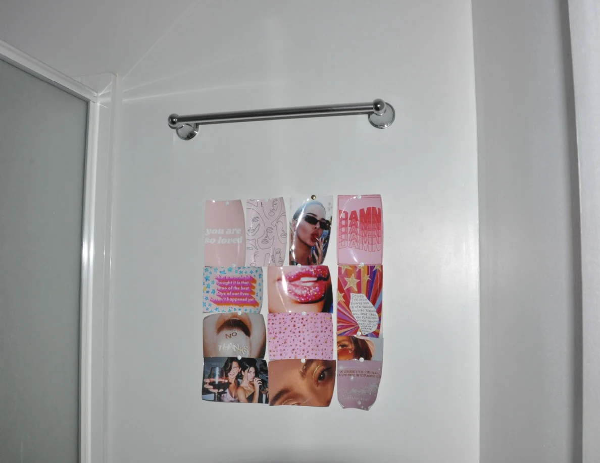Pink photo-and-text collage beneath an empty metal towel bar on a white bathroom wall.