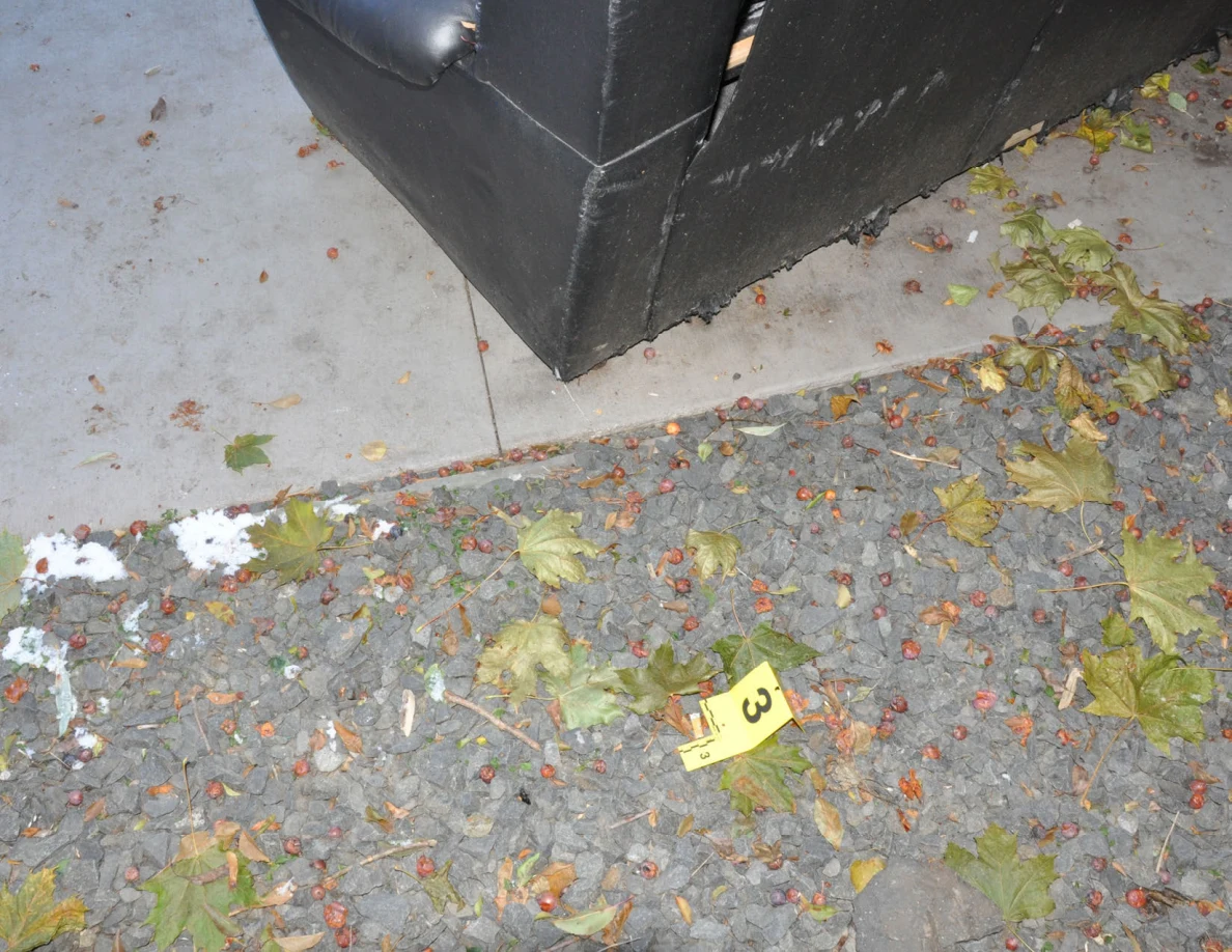 Yellow marker 3 on gravel with fallen leaves beside a sofa corner and patio edge.