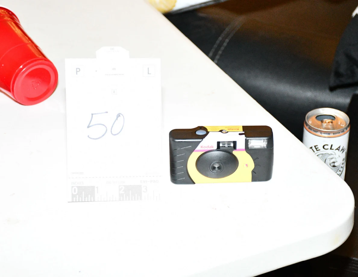 Yellow-and-black disposable camera on a white table beside card 50, a red plastic cup and a beverage can.