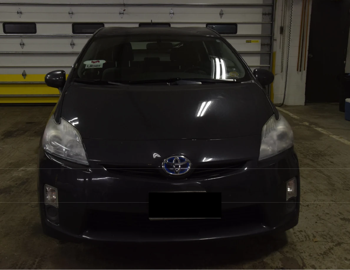 Front of a dark blue Toyota Prius inside a garage, with the license plate blacked out.