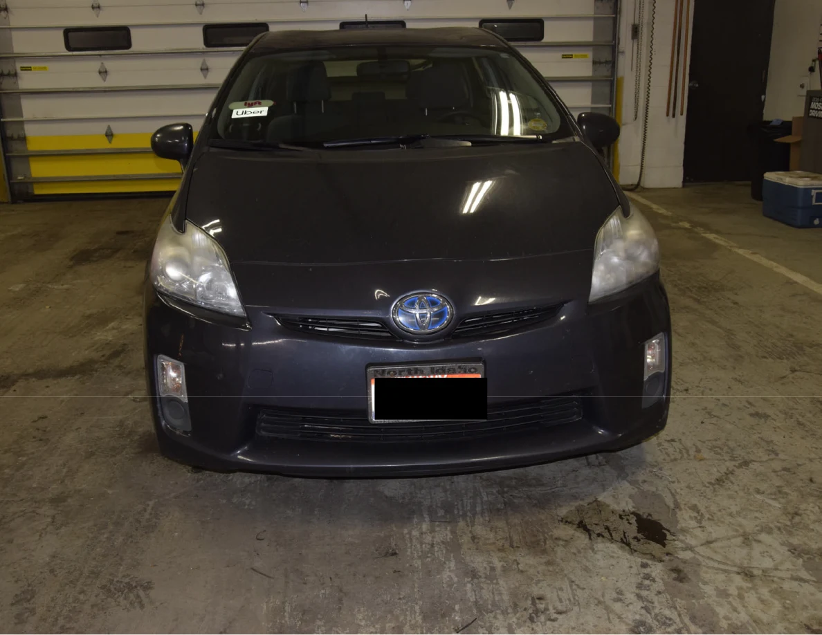 Front view of a dark blue Toyota Prius on a garage floor, with a blacked-out license plate.