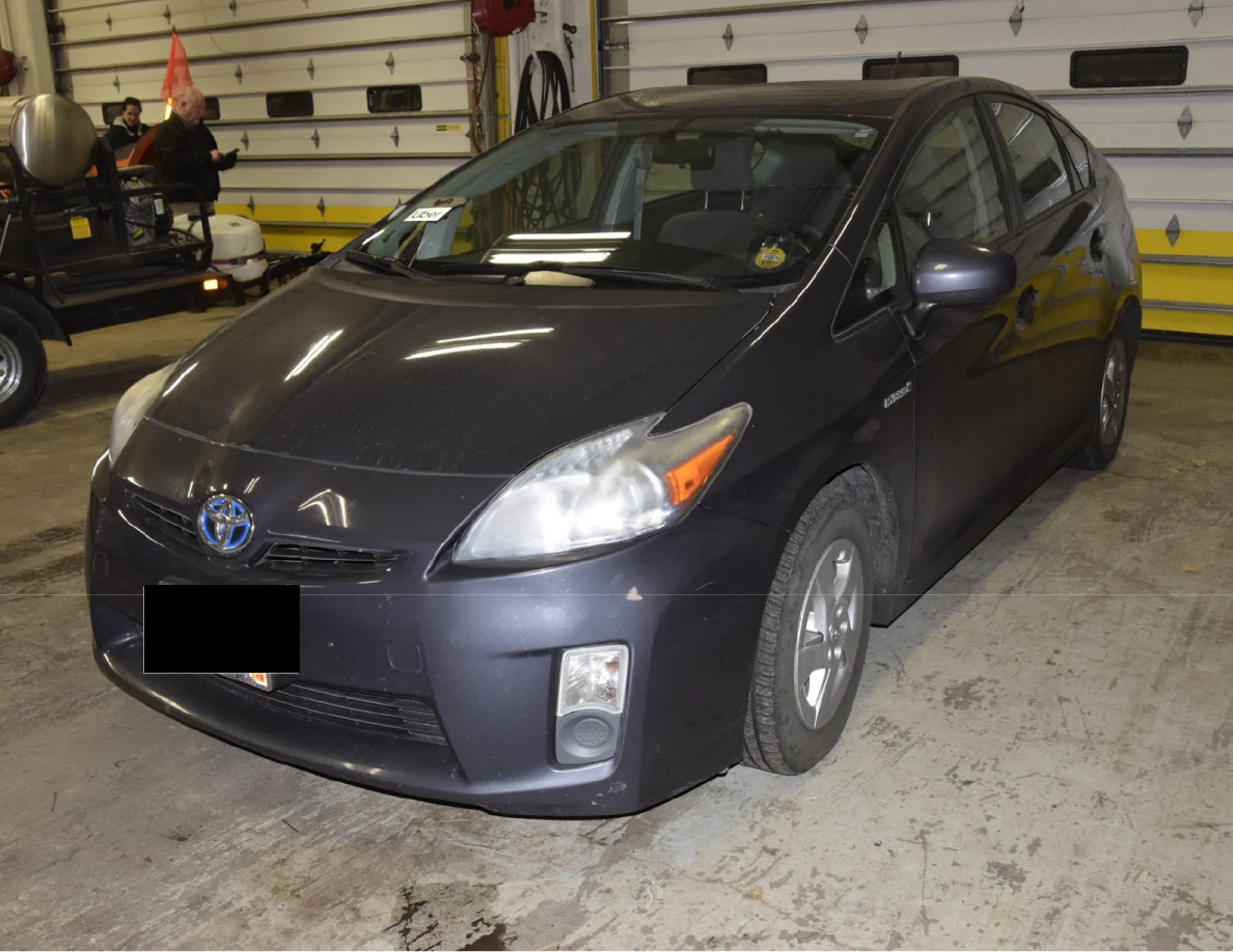 Front corner of a dark blue Toyota Prius inside a garage, with a blacked-out license plate.