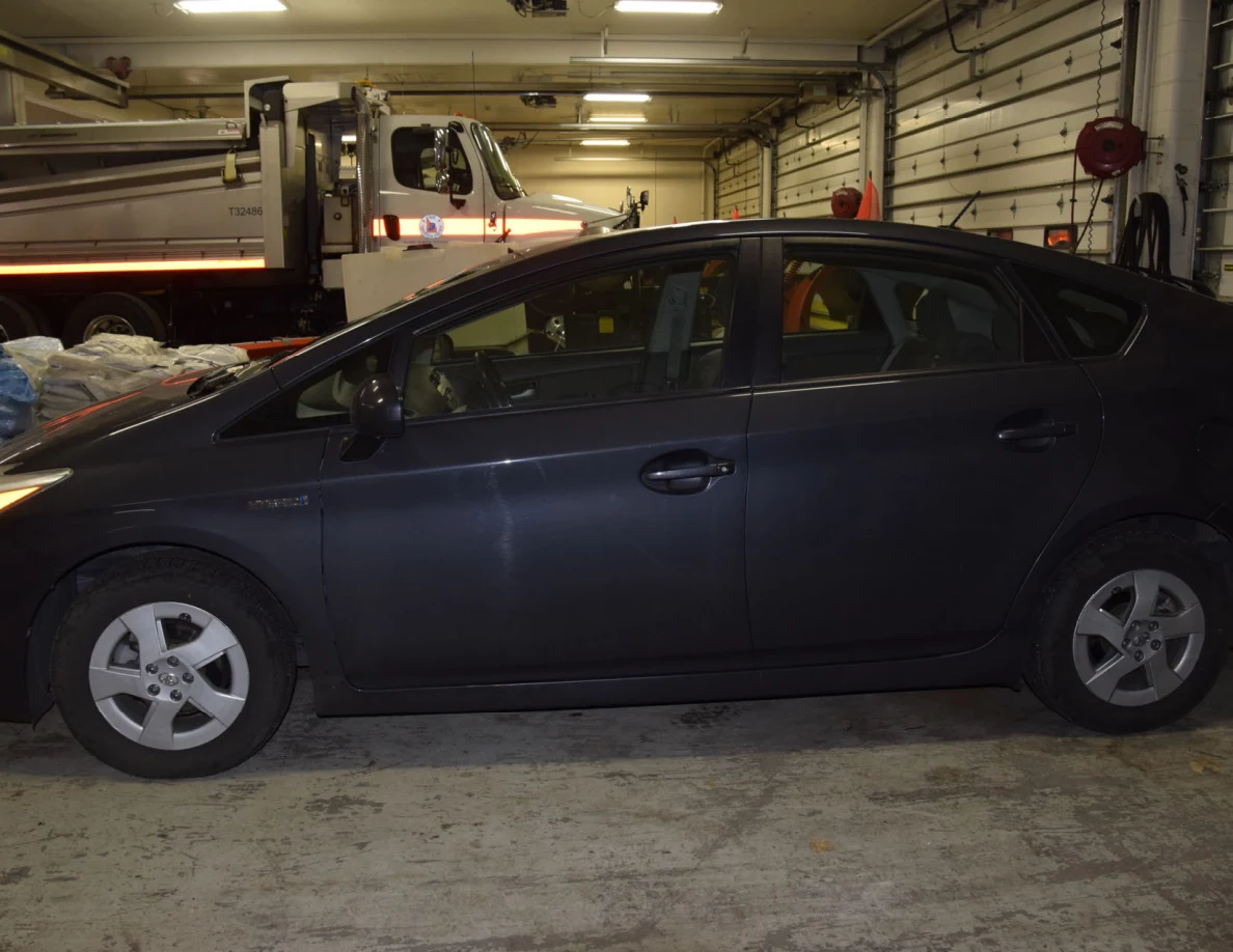 Side view of a dark blue hatchback in a garage, with a truck behind it.
