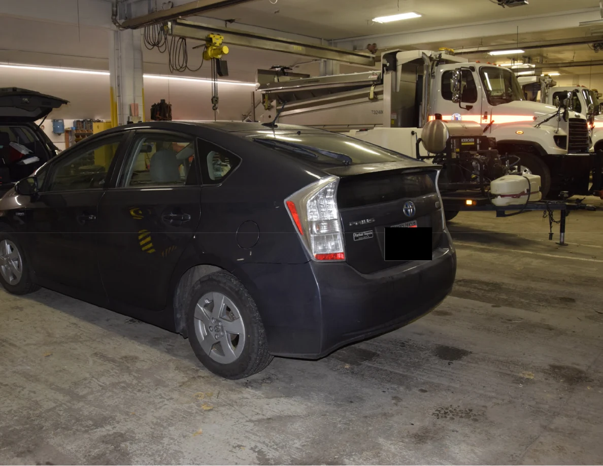 Rear corner of a dark blue Toyota Prius in a garage, with a blacked-out license plate.