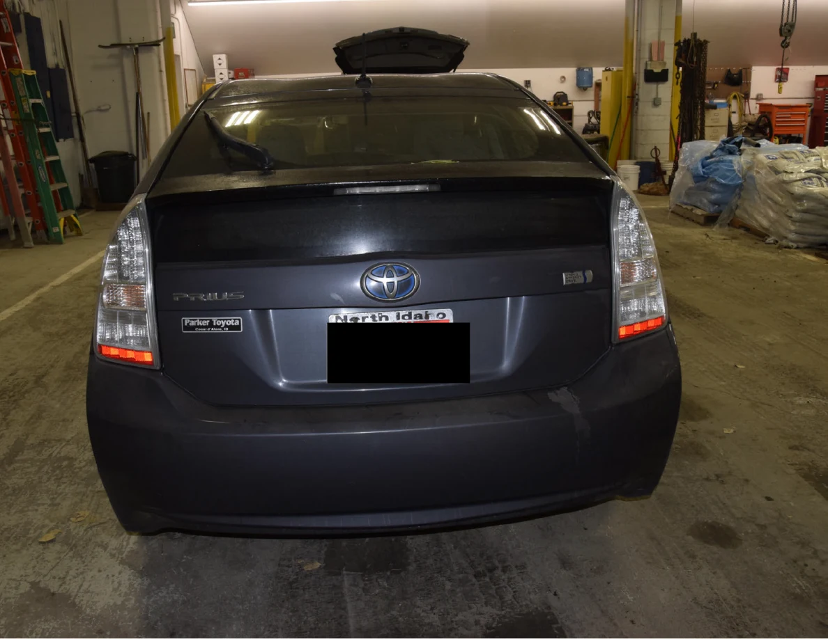 Rear of a dark blue Toyota Prius with a blacked-out license plate inside a garage.