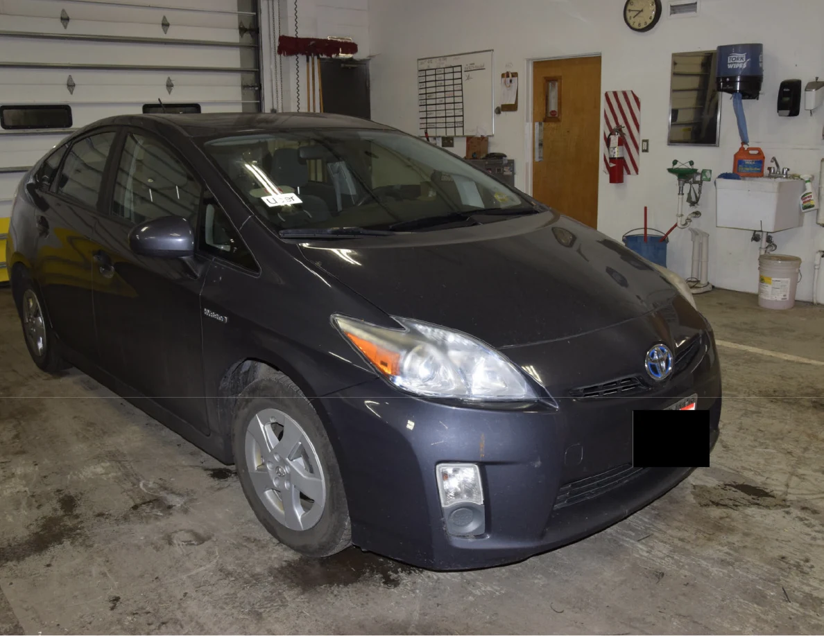 Front corner view of a dark blue Toyota Prius beside a garage sink, with a blacked-out license plate.