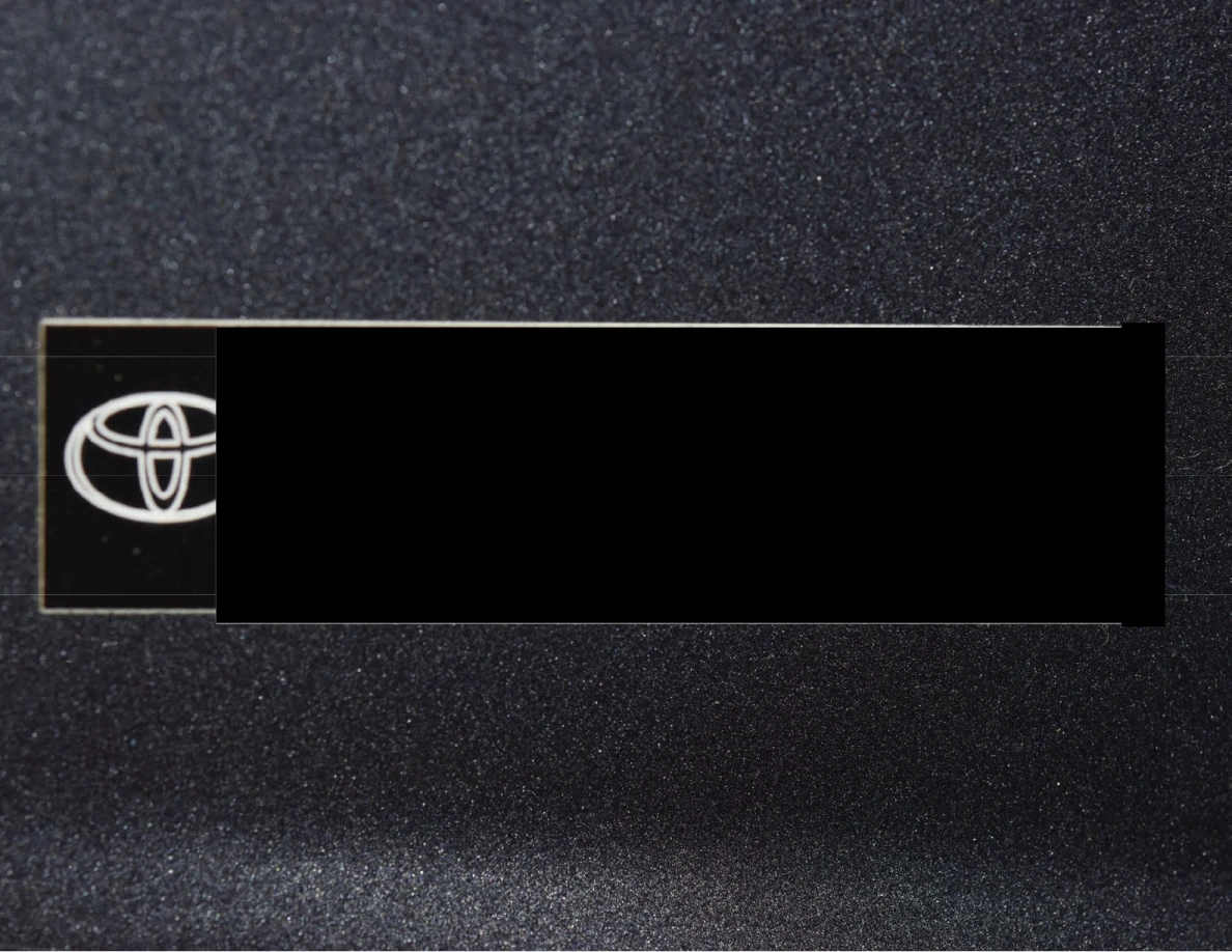 Close view of a Toyota label on dark painted bodywork, with most of the label blacked out.