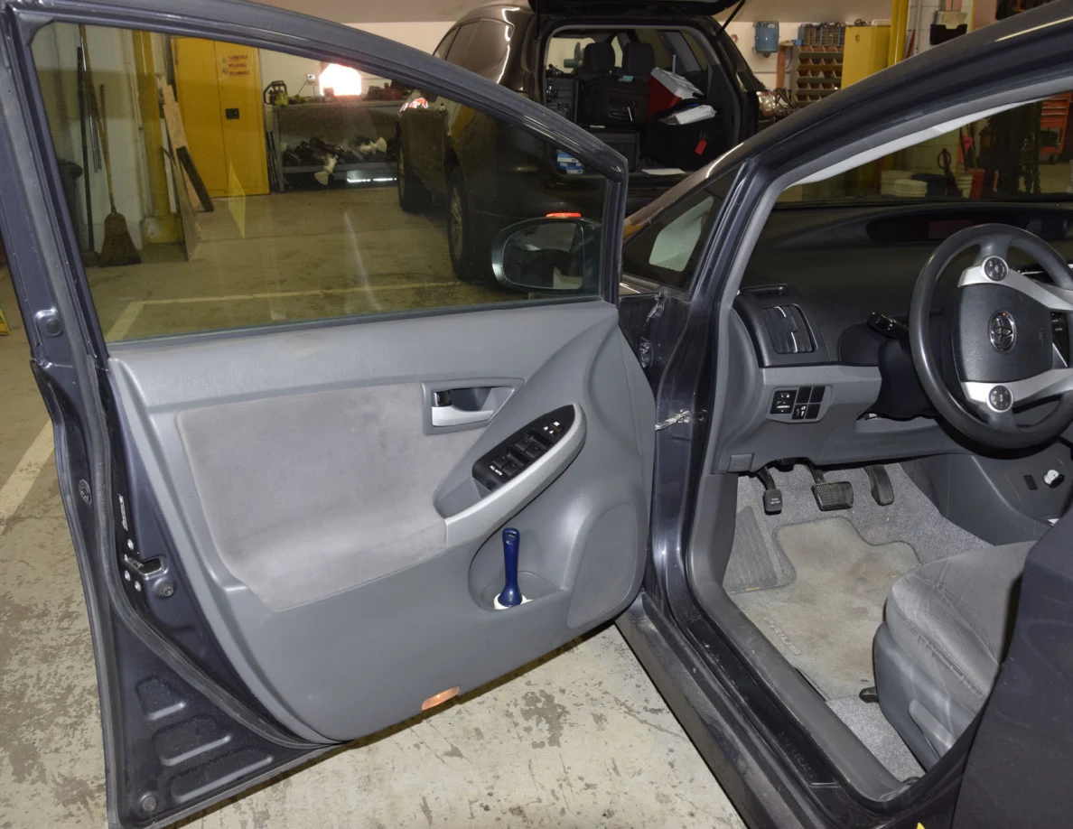 Open driver door showing gray interior trim, window switches, blue flashlight and steering wheel.