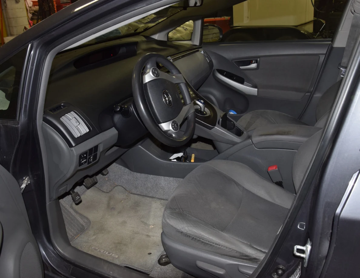 Driver seating area with gray fabric seat, steering wheel, pedals, floor mat and center console.