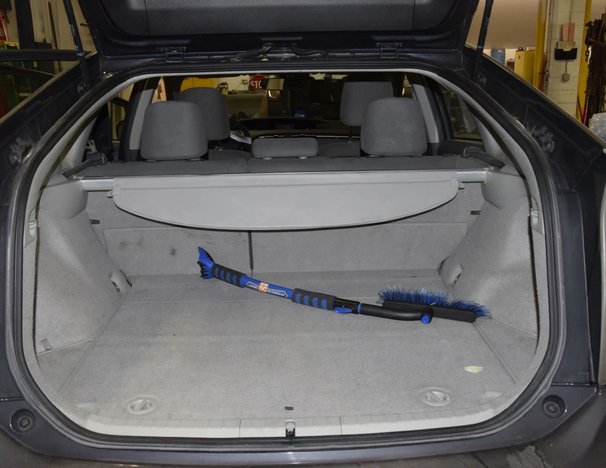 Open hatch cargo area with a blue snow brush and ice scraper on gray carpeting.