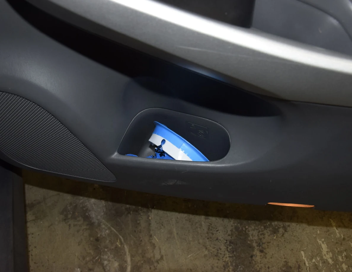 Close view of a blue-and-white container in the lower pocket of a gray car door.