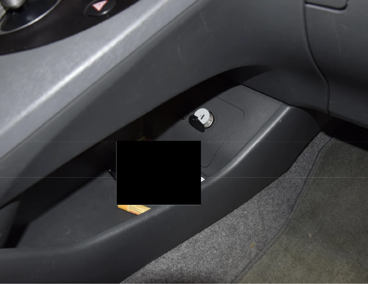 Lower car center-console storage tray with a charging adapter and a black redaction over an item.