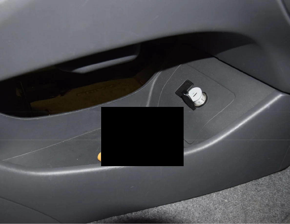 Closer view of center-console storage and a charging adapter, with an item blacked out.