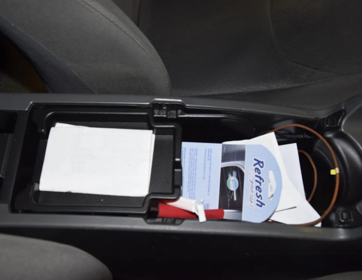 Open center armrest storage containing packaging, papers and cables.