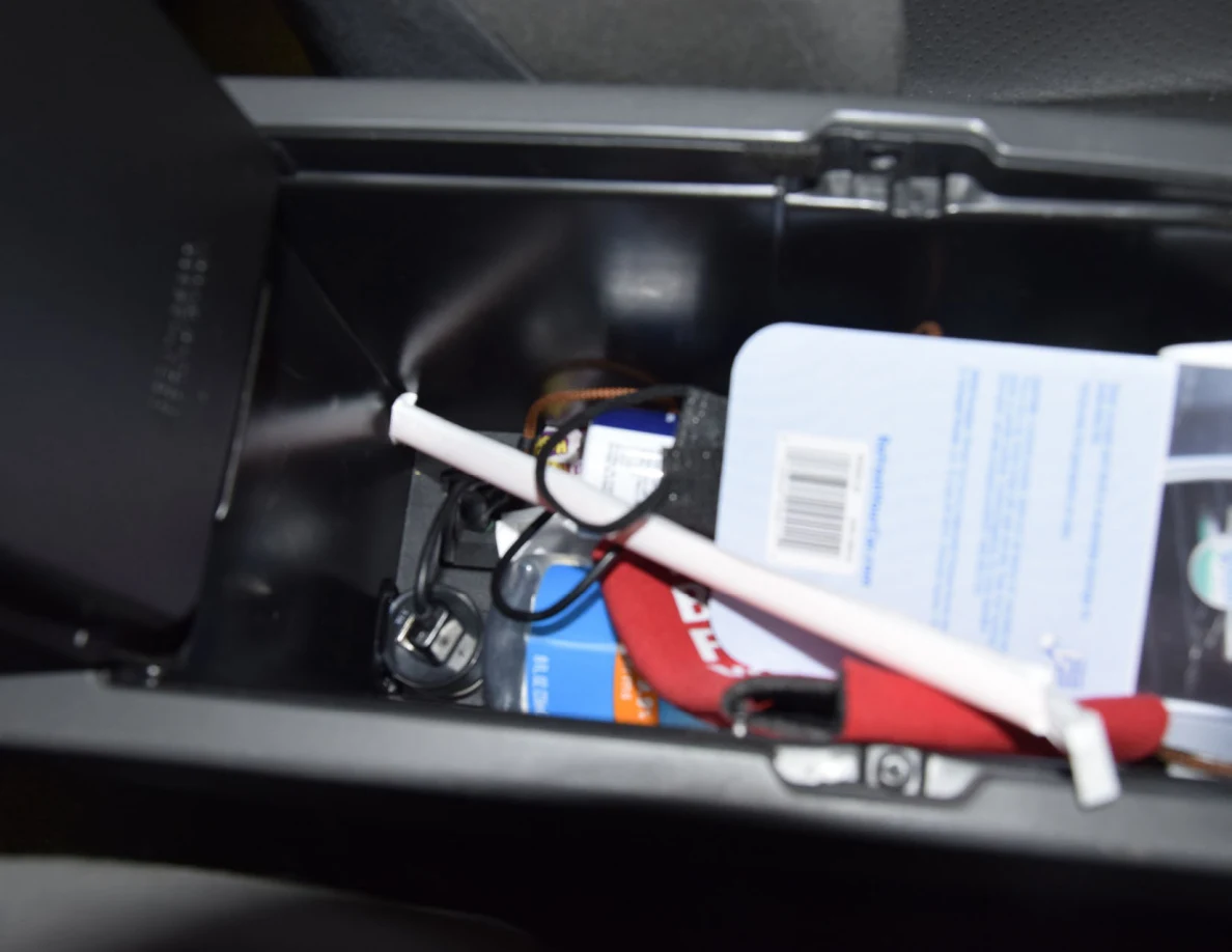 Close view inside center-console storage with packaging, a white tube, red strap and cables.