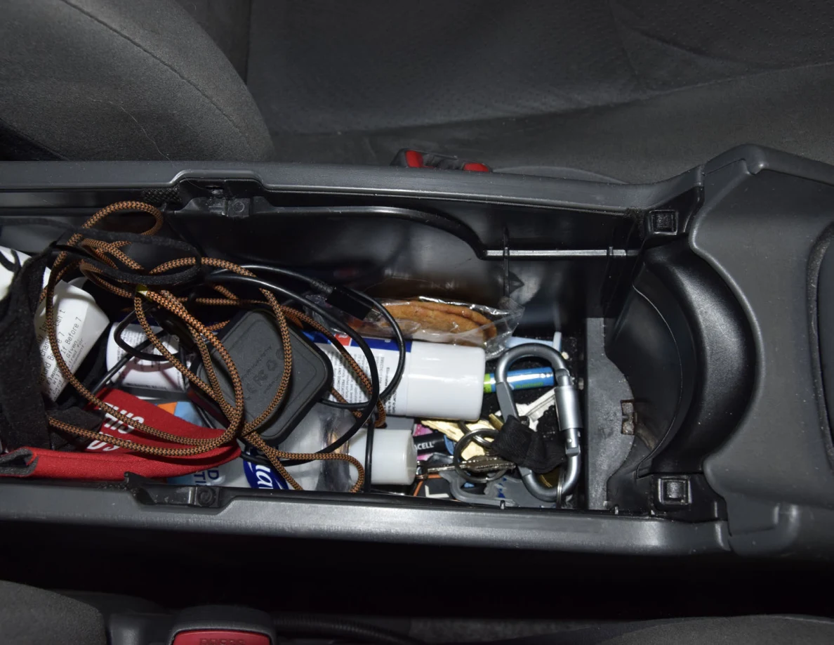 Wider view of keys, cords, charging adapters and small containers inside center-console storage.