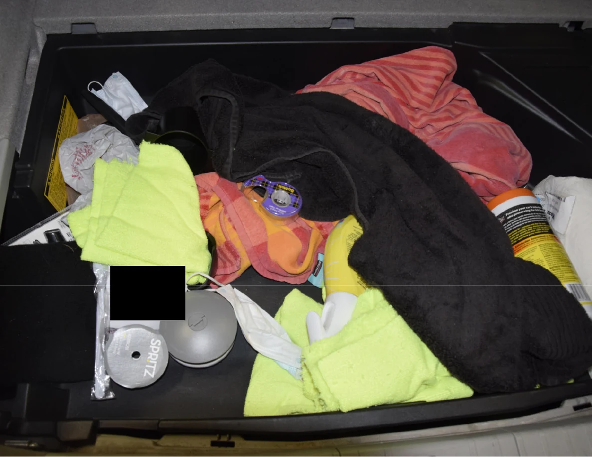 Open hatch storage with brightly colored cloths, black fabric, small containers and a black redaction.