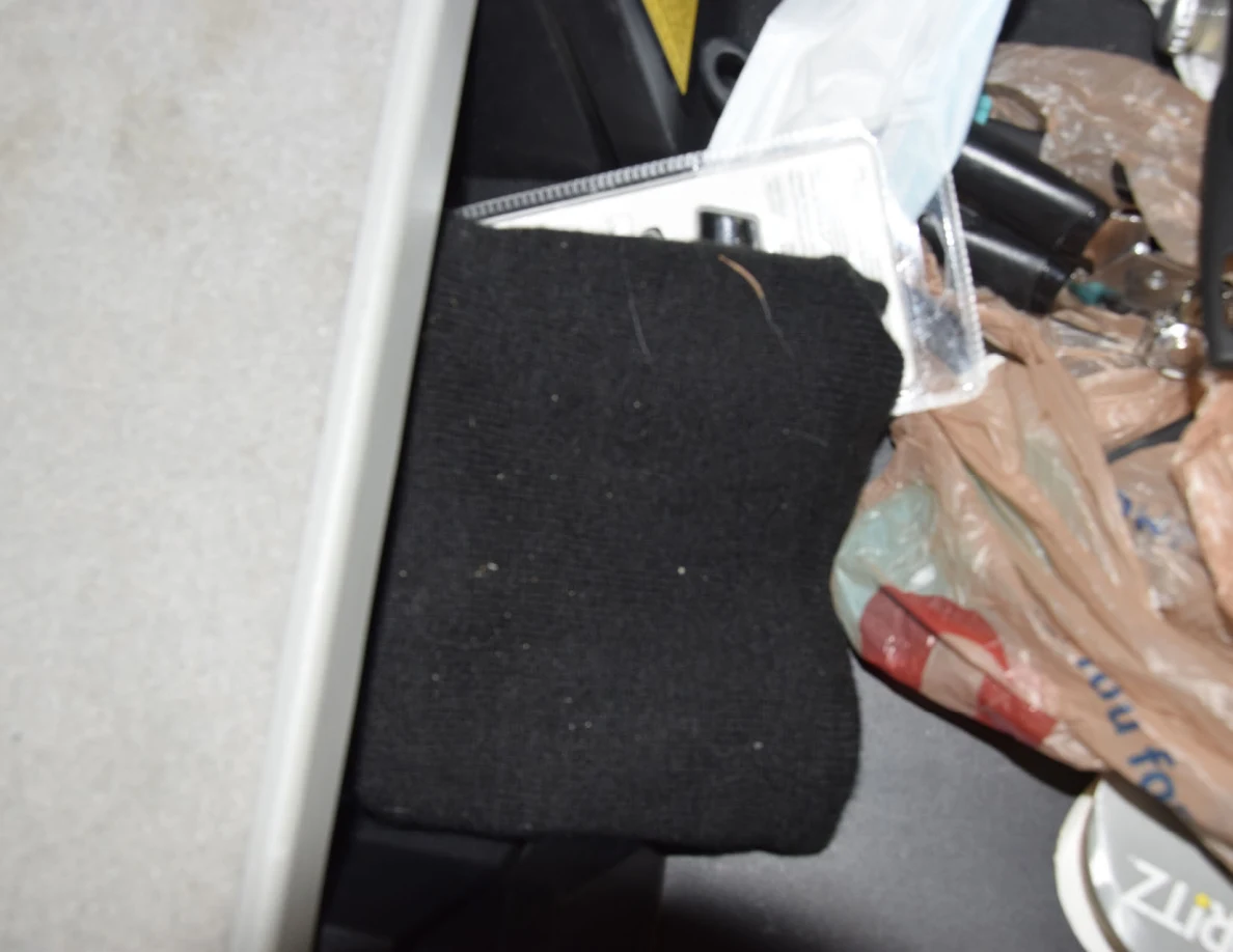 Close view of black knit fabric beside plastic shopping bags, packaging and a disposable face mask.