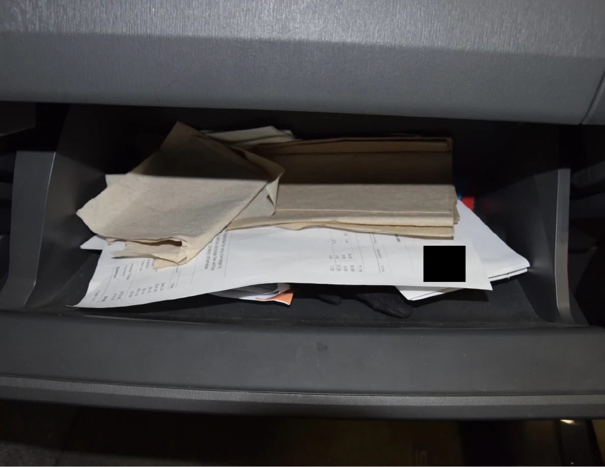 Open glove compartment with brown napkins and papers, with a small black redaction.