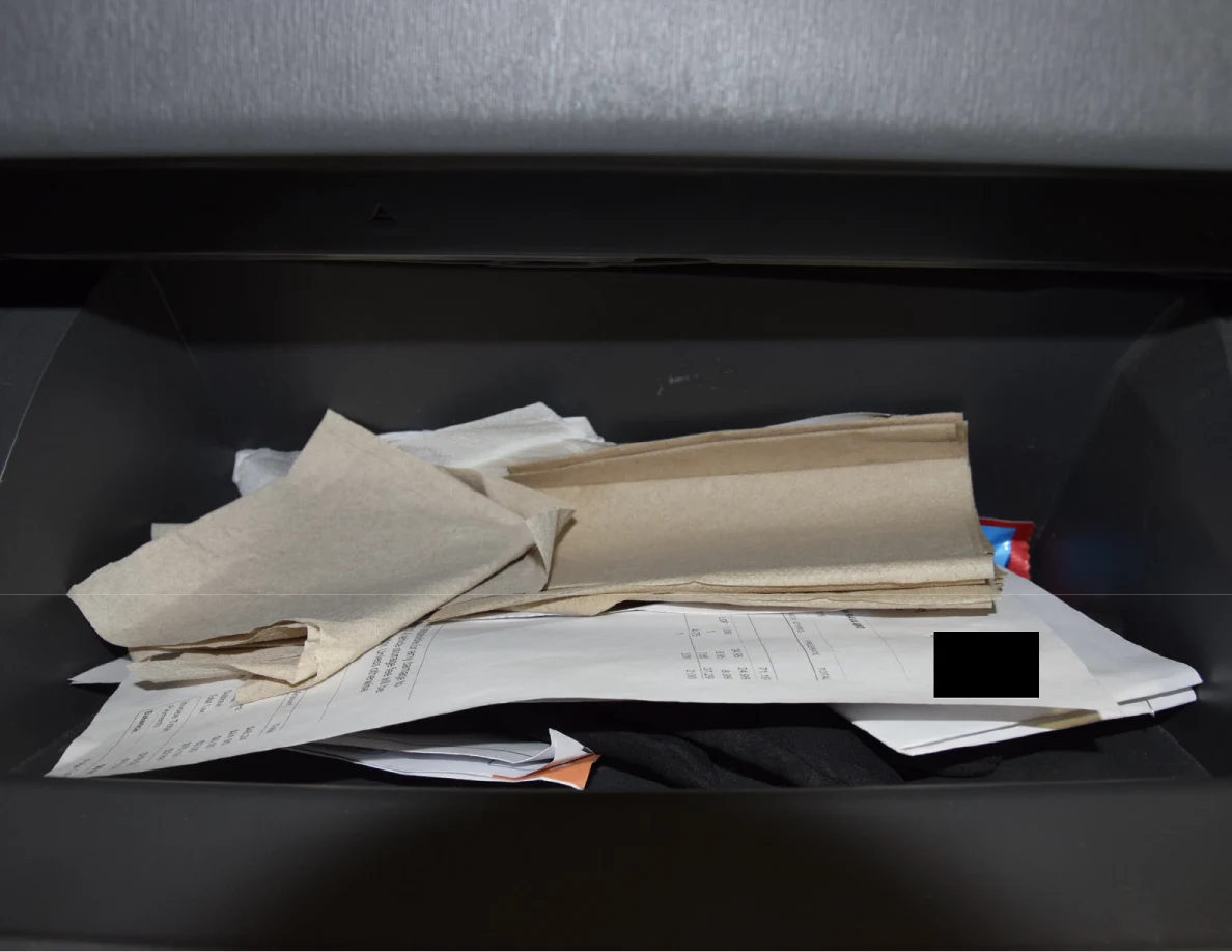 Closer view of napkins and papers in a glove compartment, with a small black redaction.