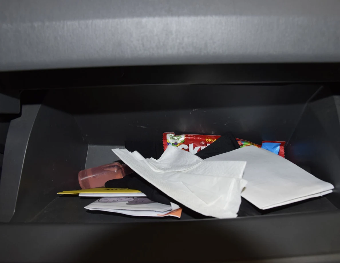 Glove compartment containing white tissues, papers and a red candy package.