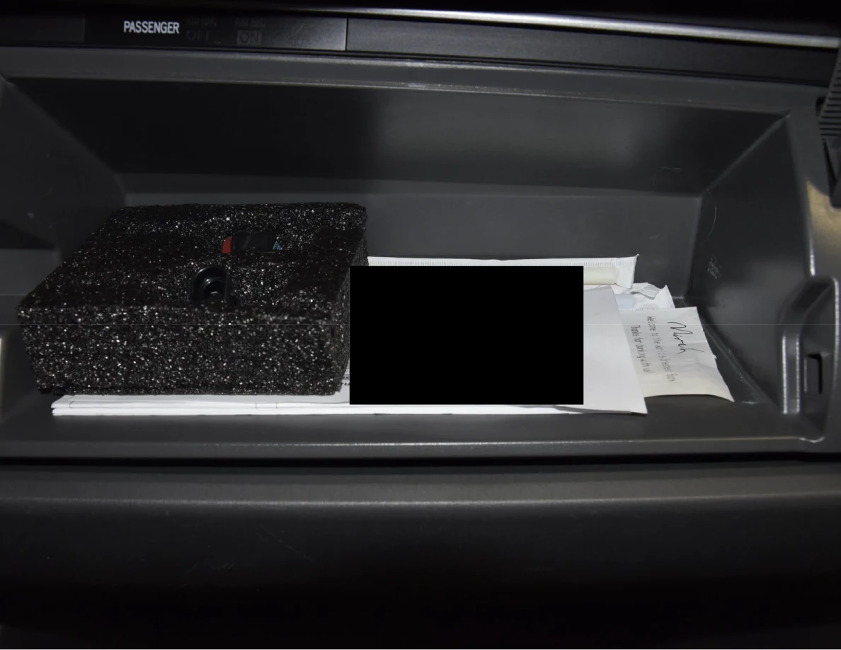 Upper dashboard storage with a black foam block and papers, some blacked out.