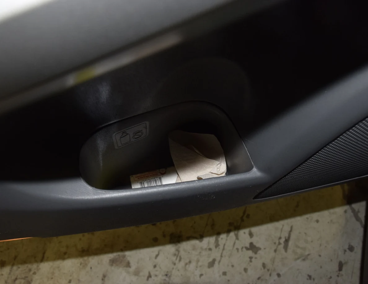 Lower car-door pocket with folded paper and a small cylindrical container.