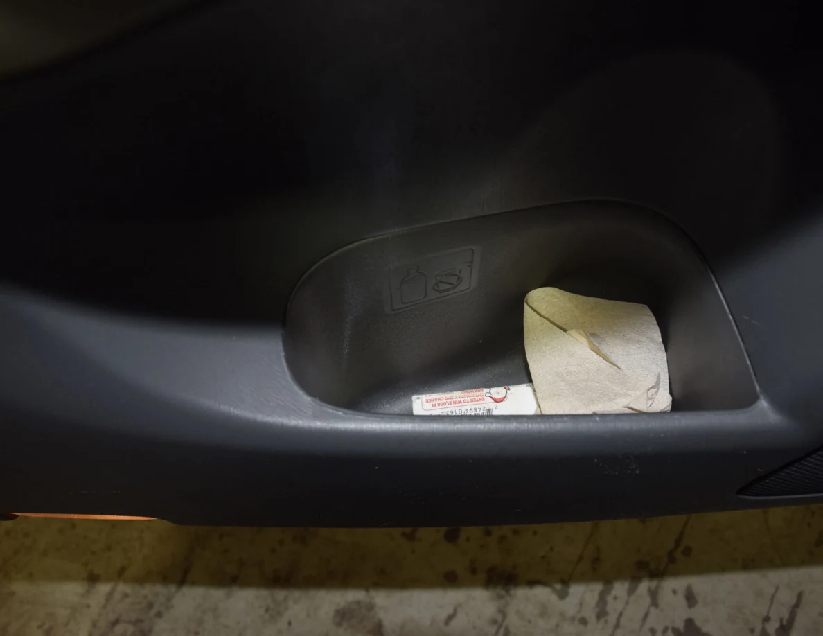 Close view of folded paper and a small cylindrical container inside a car-door pocket.