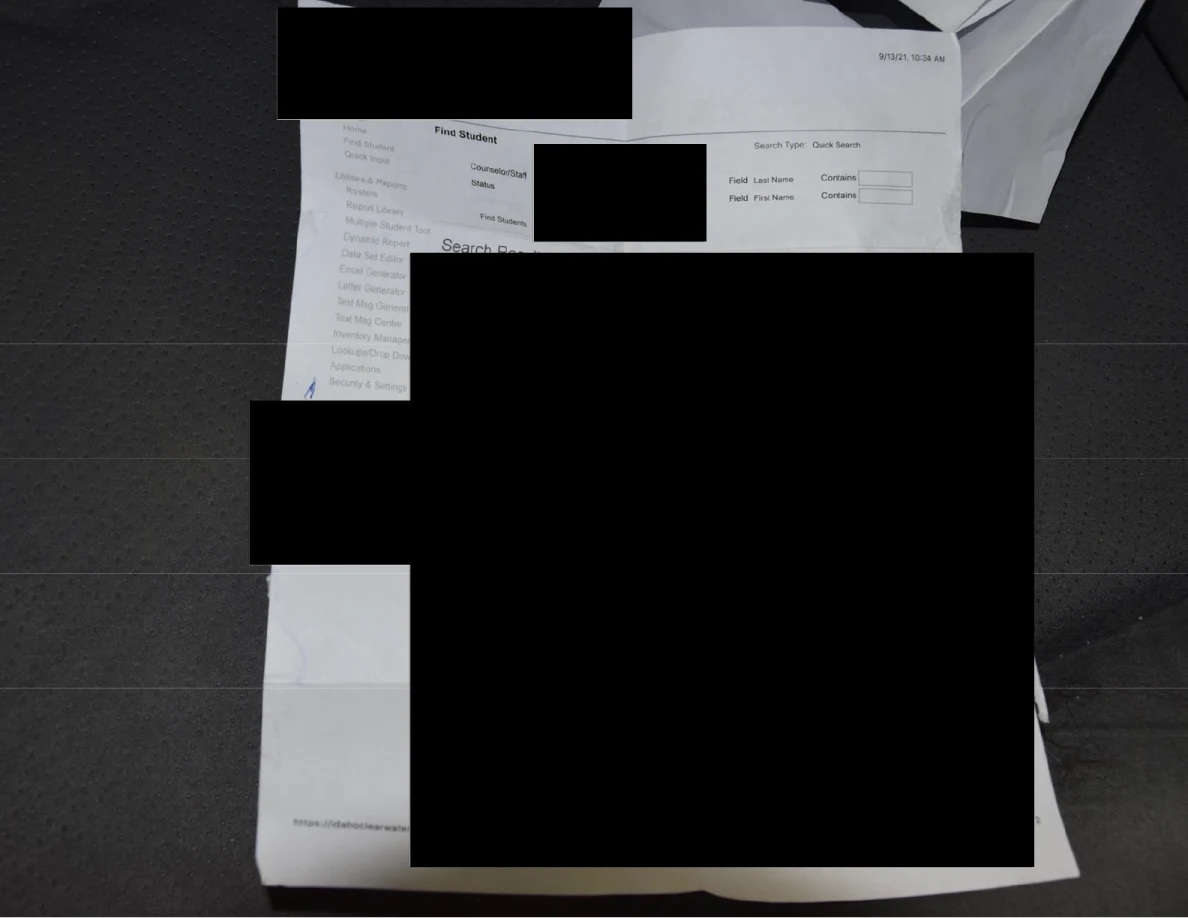 Printed sheet on gray car upholstery with large black redactions covering most text.