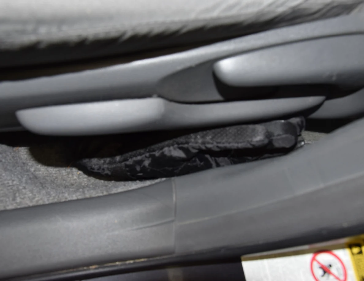 Black glove tucked beside the base of a gray car seat and door sill.