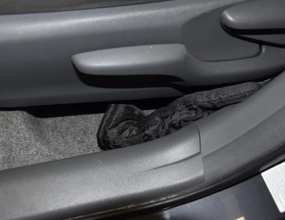 Black glove on the carpet between a gray car seat and door sill.
