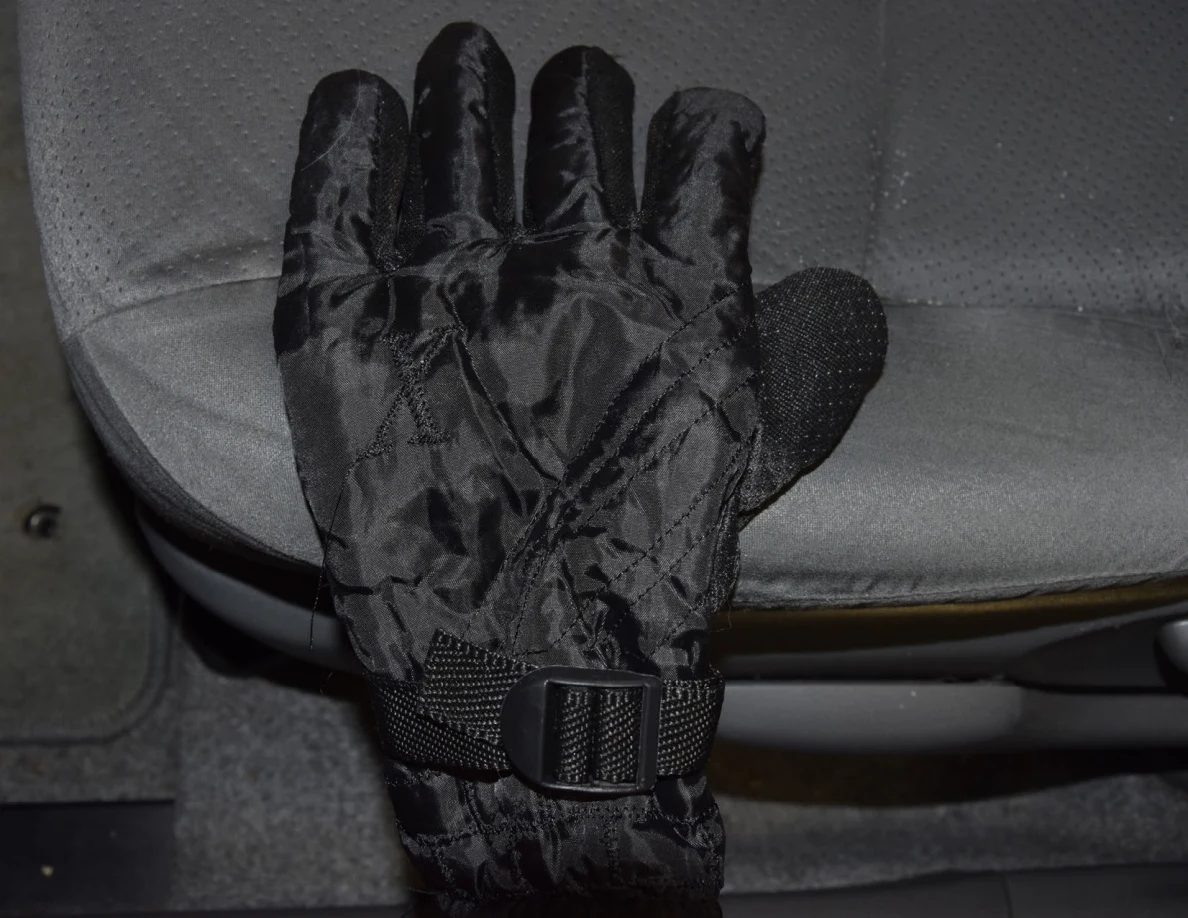 Back of a black insulated glove with wrist buckle laid on a gray car seat.