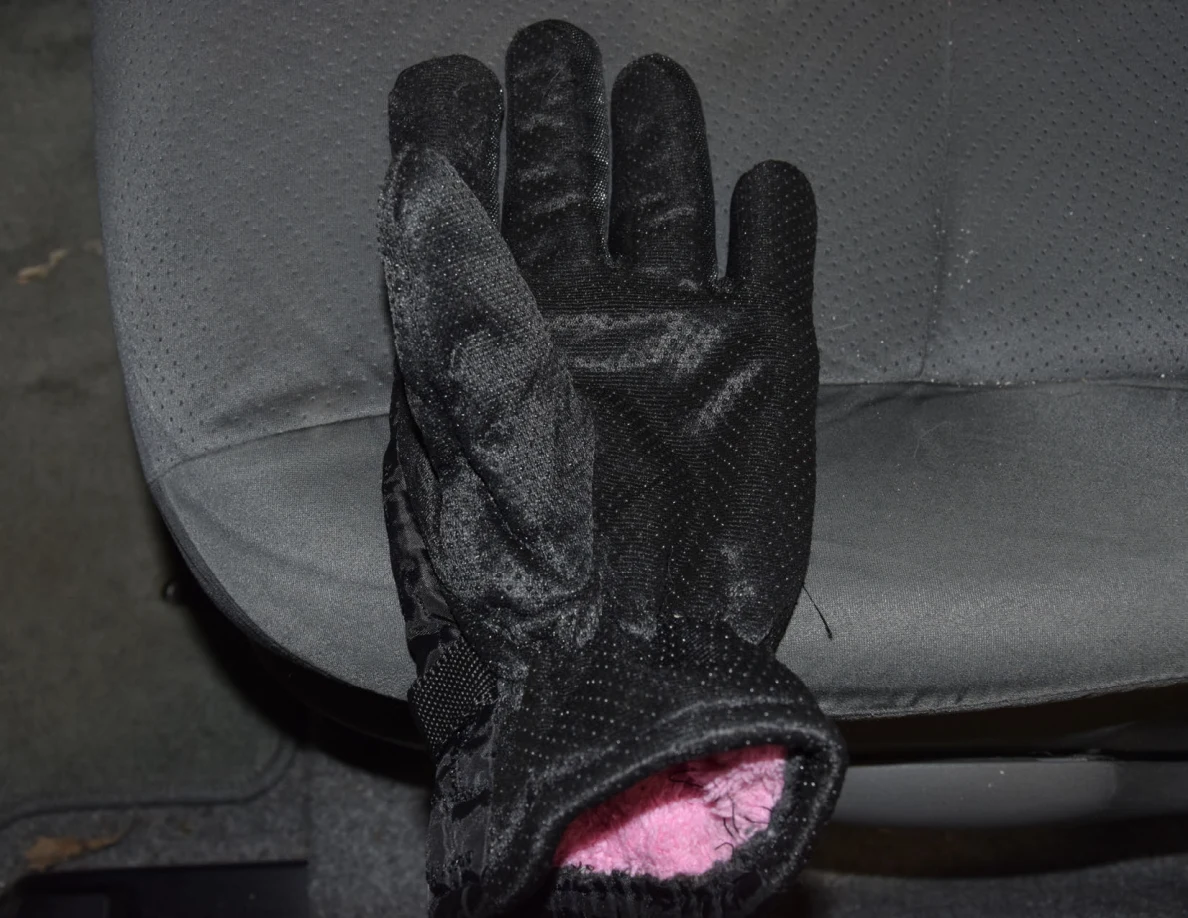Palm of a black glove with textured grip and pink lining at the cuff, on a gray car seat.