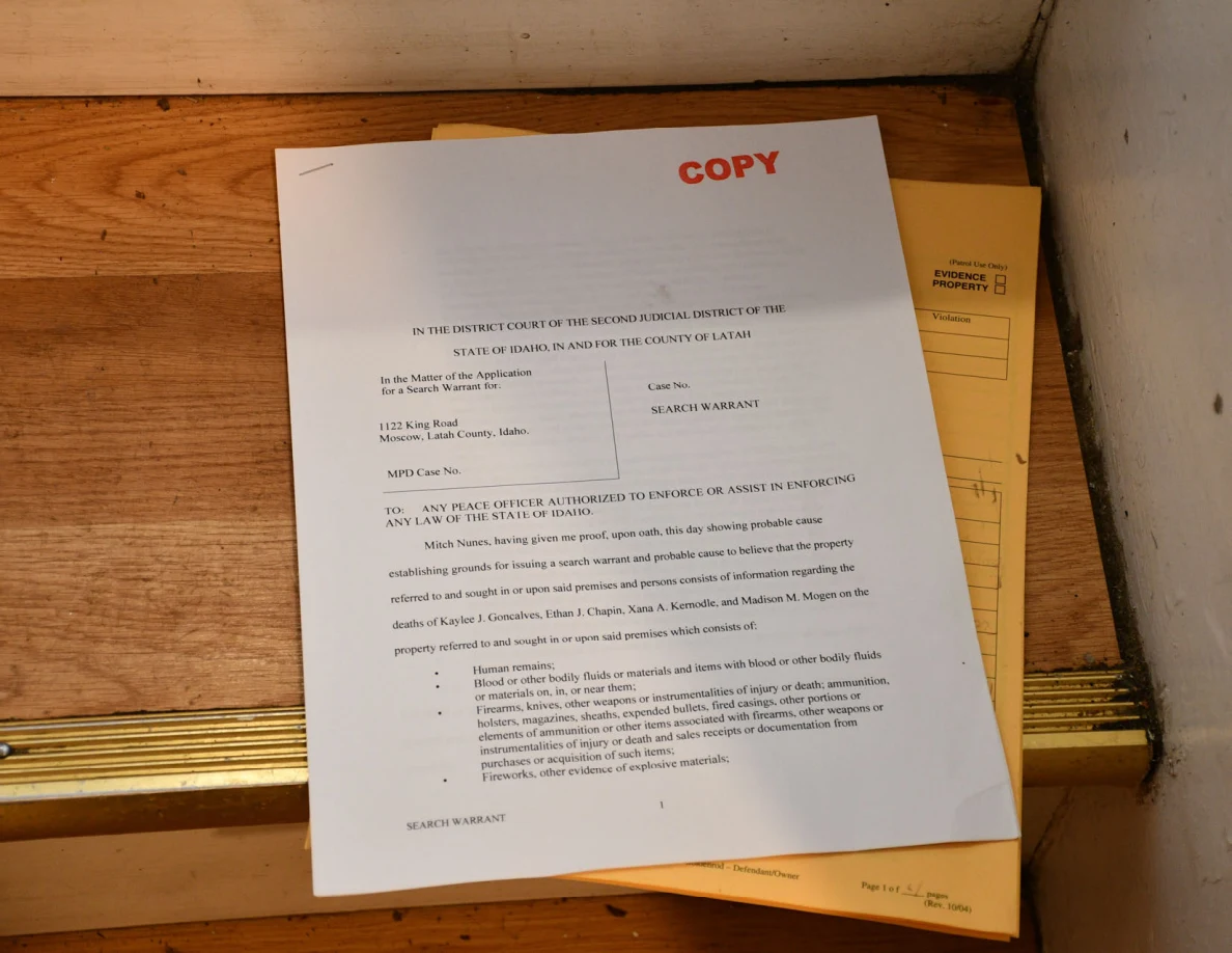 Printed search-warrant copy on a yellow envelope on a wooden stair.
