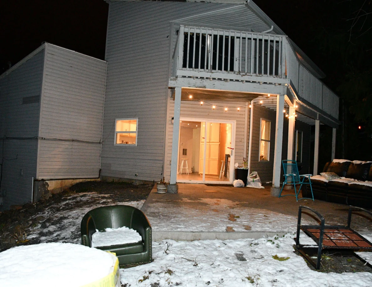 Snow-covered yard with a green chair, metal furniture frame and lit gray house with raised deck.