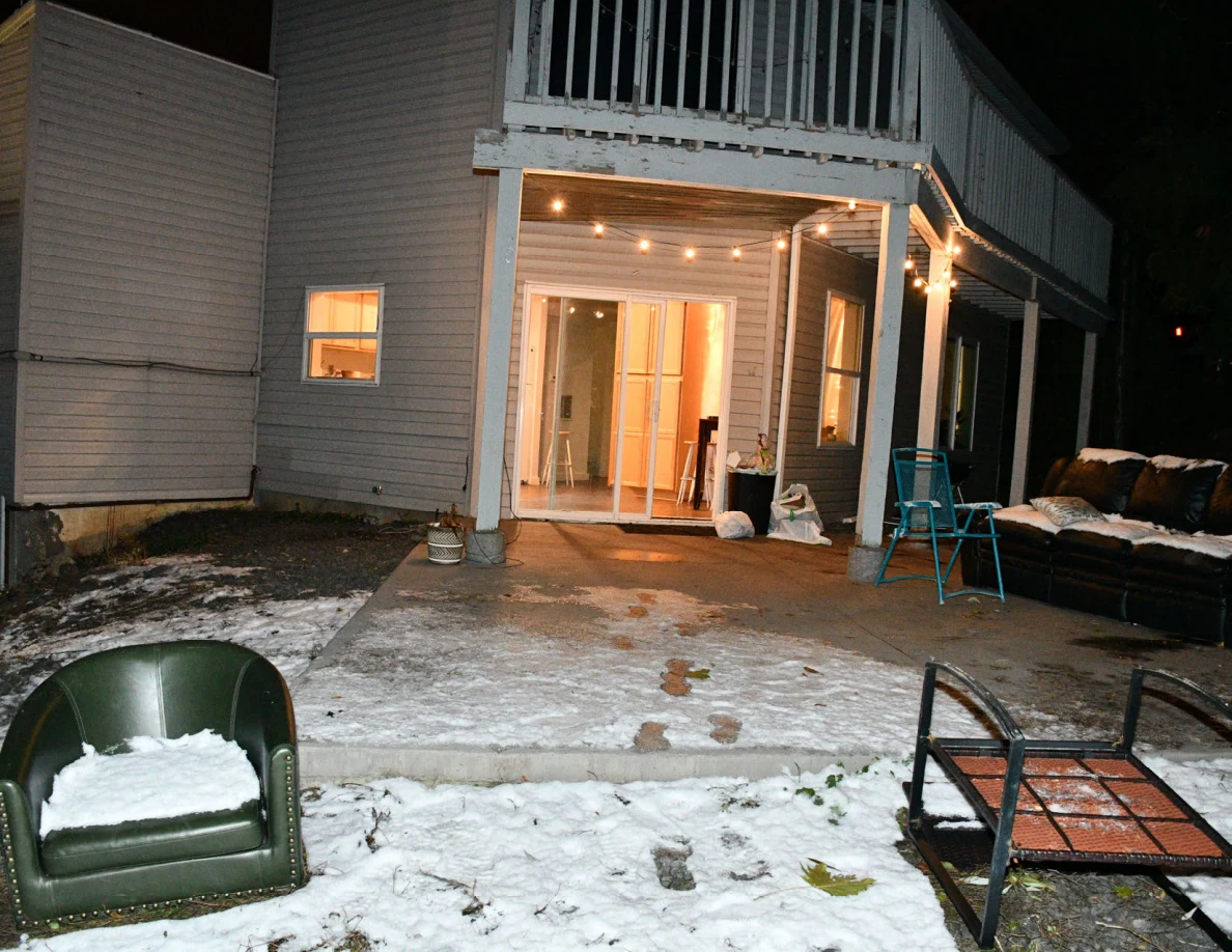 Lit sliding doorway beneath a raised deck, with green chair and metal furniture frame in snowy yard.