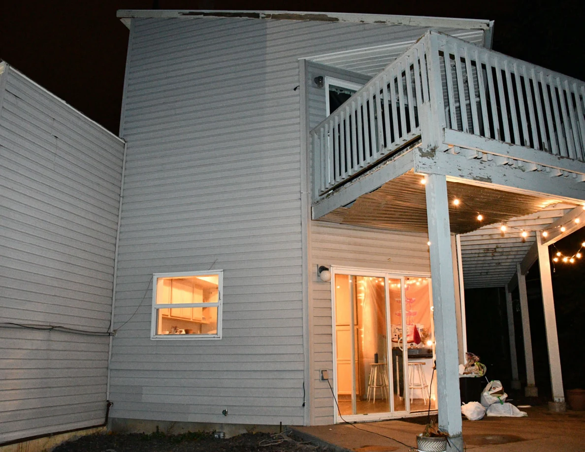 Night view of white deck railings and string lights above a lit sliding doorway.