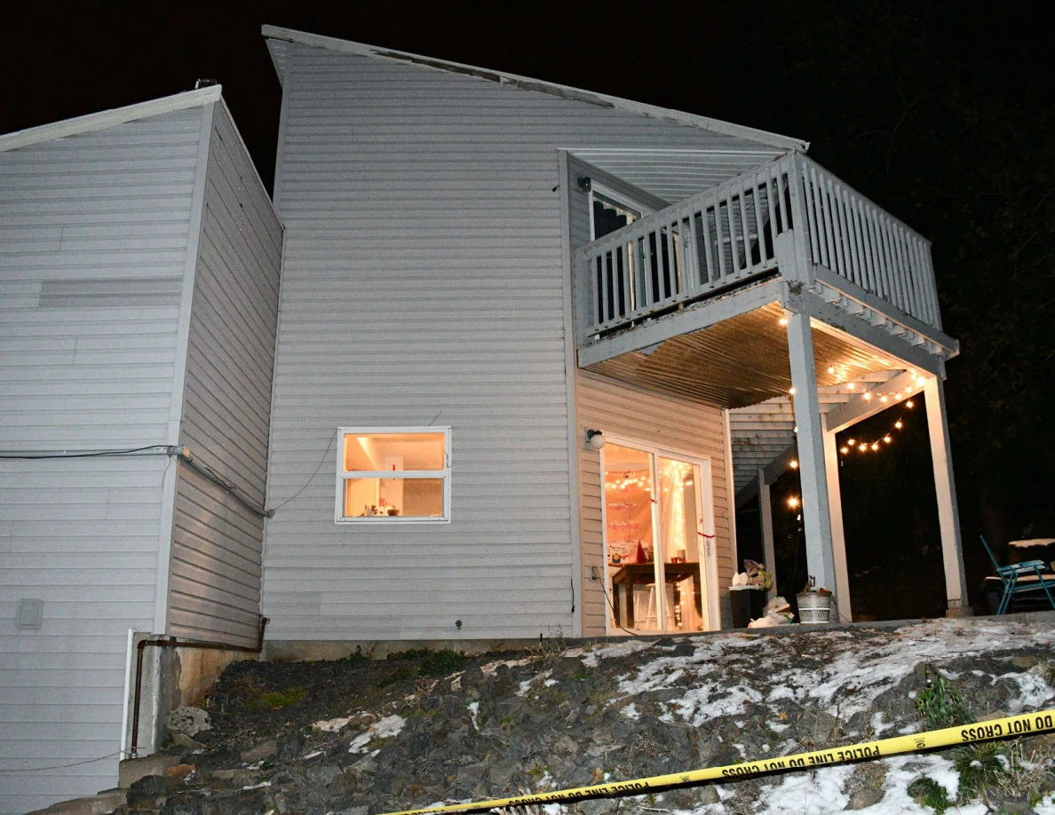 Gray house and raised deck at night, with yellow police tape crossing the snowy foreground.