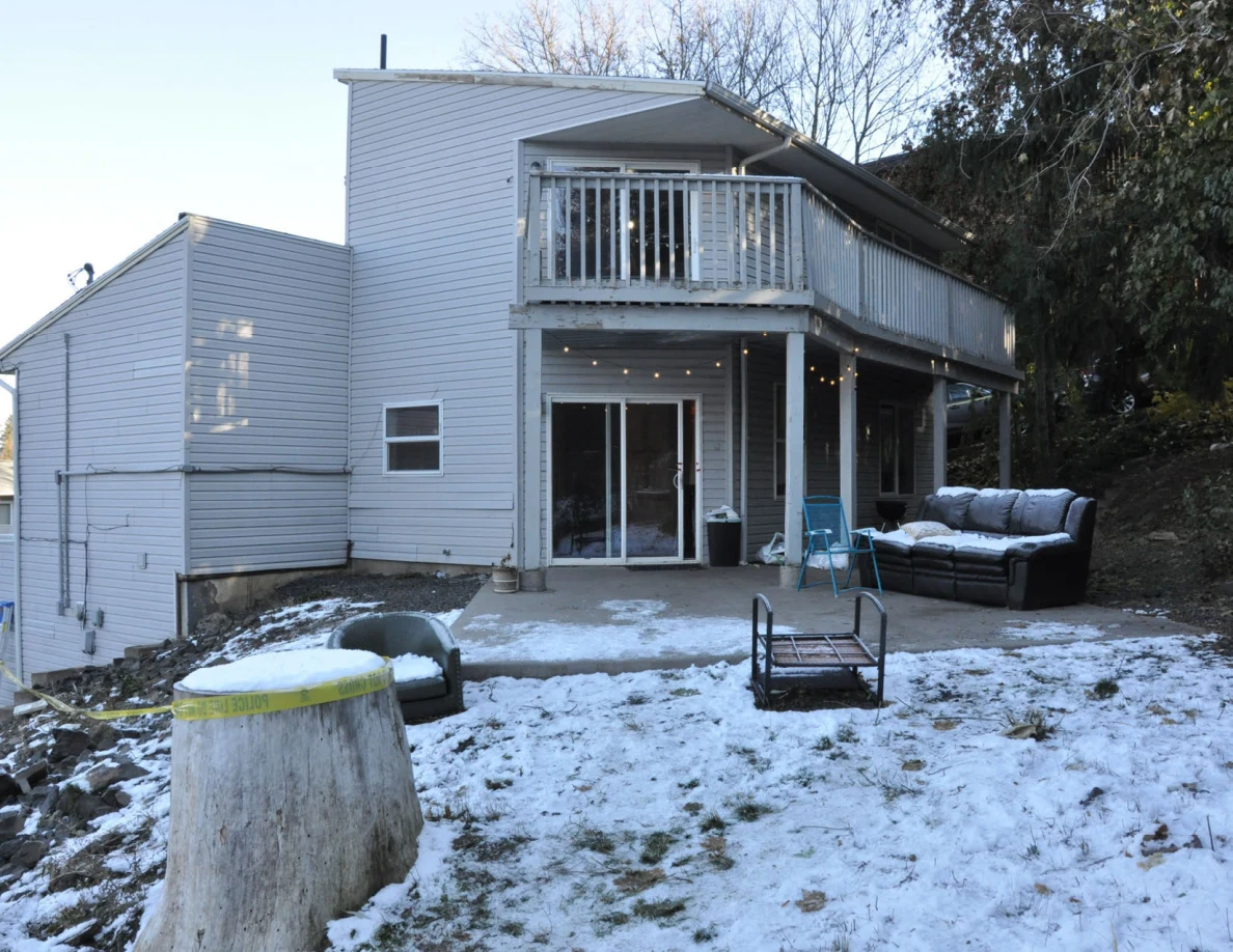 Daylight view of a gray house and raised deck overlooking a snowy yard with outdoor furniture and a large stump.