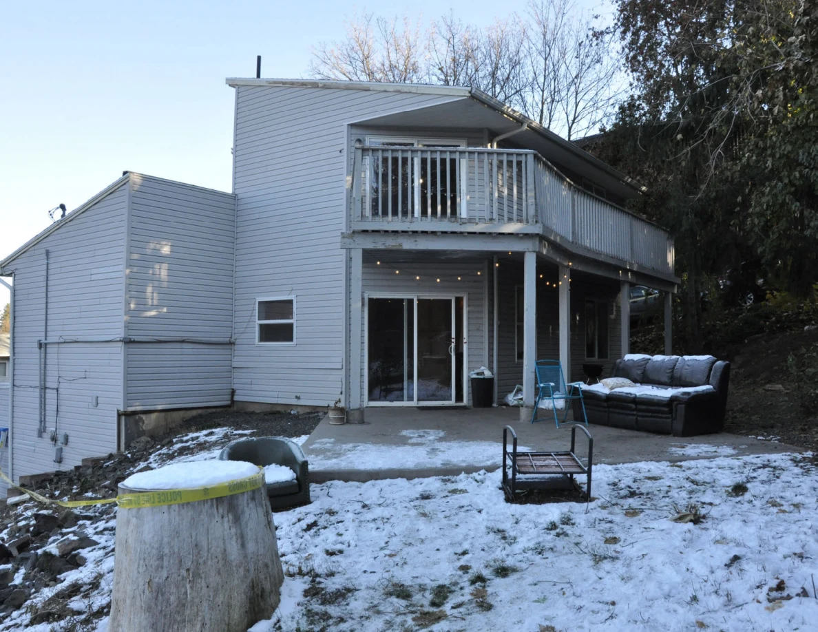 Gray house with sliding door and raised deck, snowy yard, black sofa and metal furniture frame.