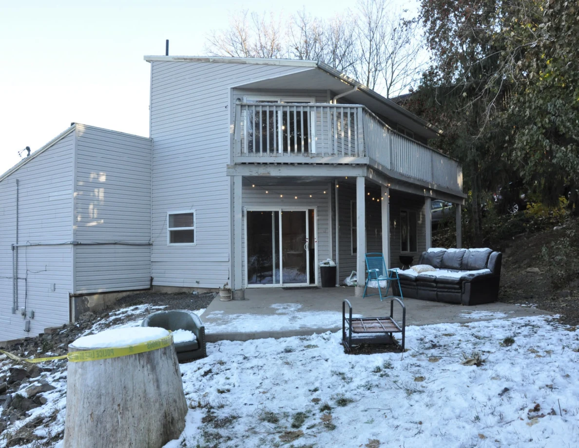 Daylight house exterior with raised deck, outdoor sofa, metal furniture frame and large stump in snowy yard.