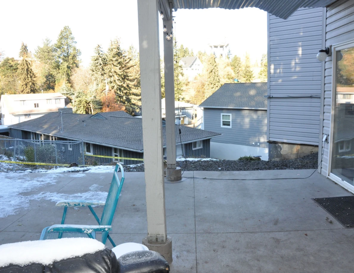Patio post and turquoise chair beside snowy ground, with neighboring houses and trees beyond.