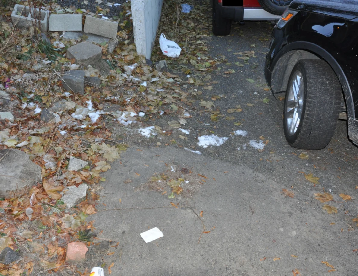 Driveway beside parked vehicles and a concrete wall, with white paper on the pavement.