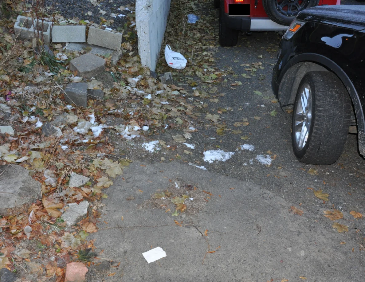 Wider view of pavement, fallen leaves, parked vehicles and a white paper on the ground.