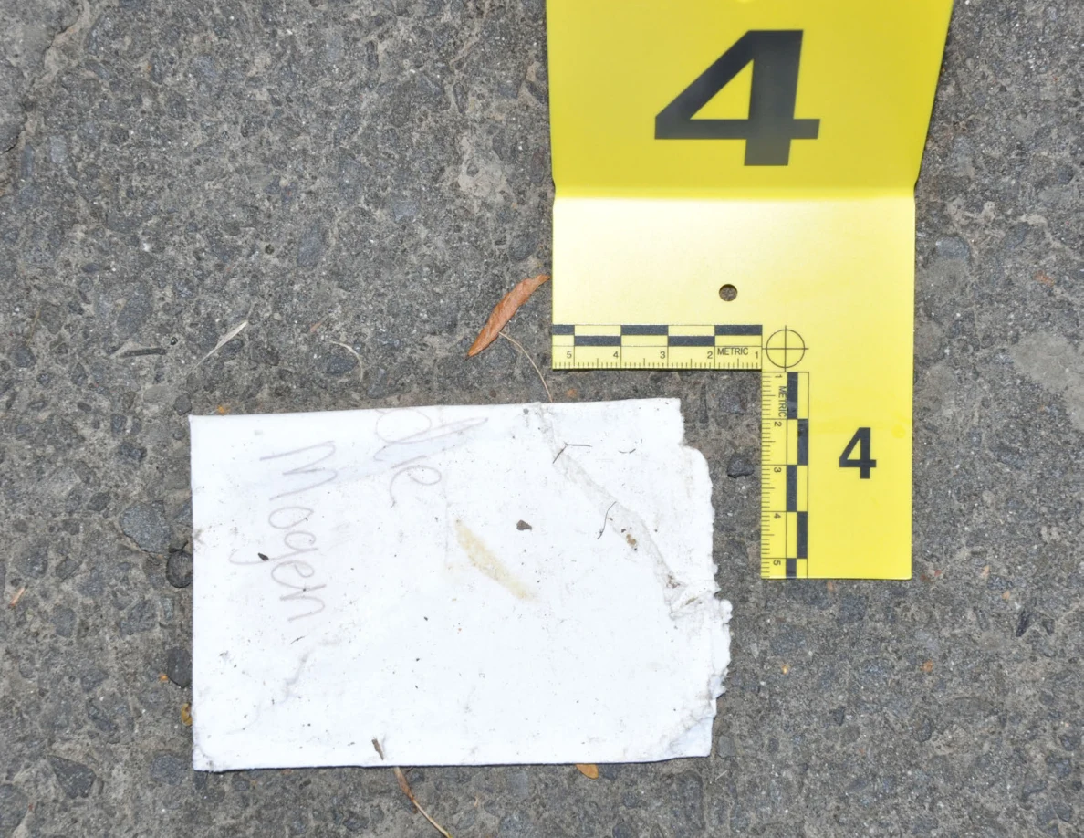 Close view of a torn white paper with faint handwriting beside yellow marker 4 and measurement scale.