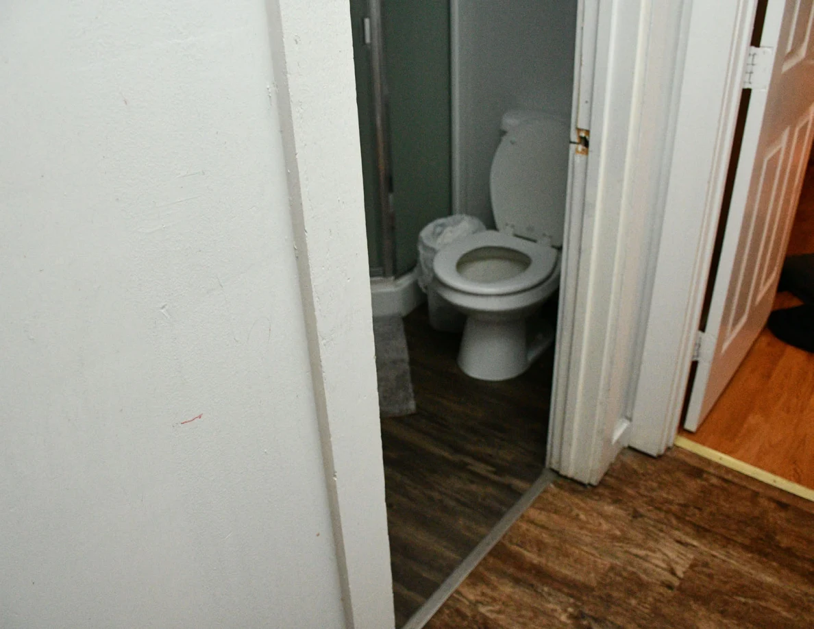 Pale hallway wall with a small reddish mark beside an open bathroom doorway and toilet.