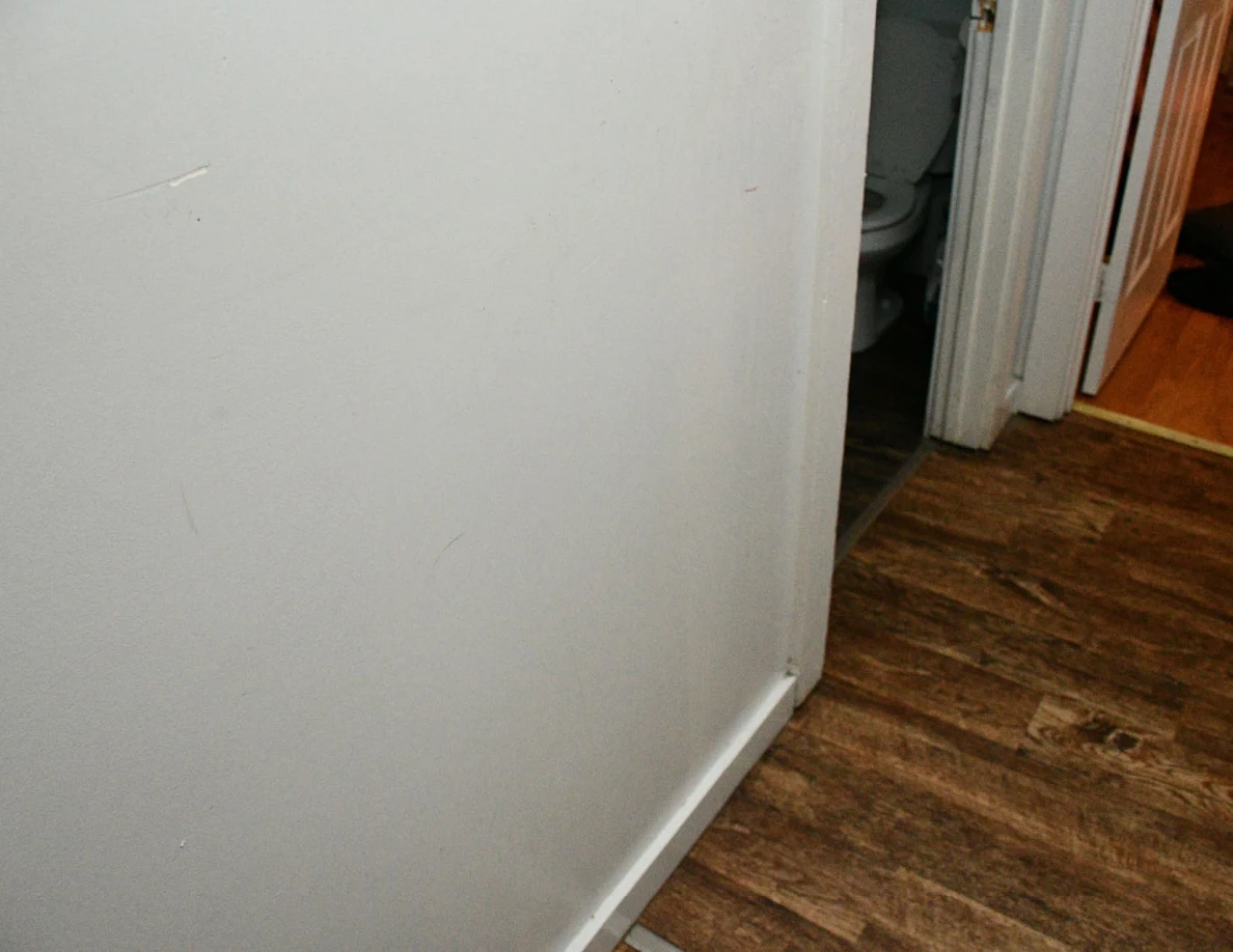Hallway wall and wood-look floor beside a bathroom doorway.
