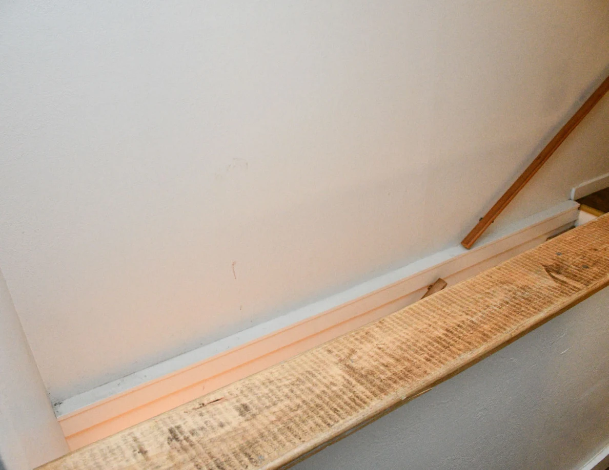 Stairwell wall and wood-capped half-wall with scuffs visible on the wood surface.