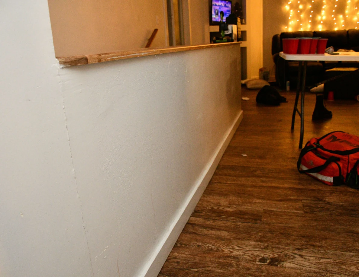 Hallway alongside a stair half-wall, with a red bag, table, red cups and decorative string lights beyond.